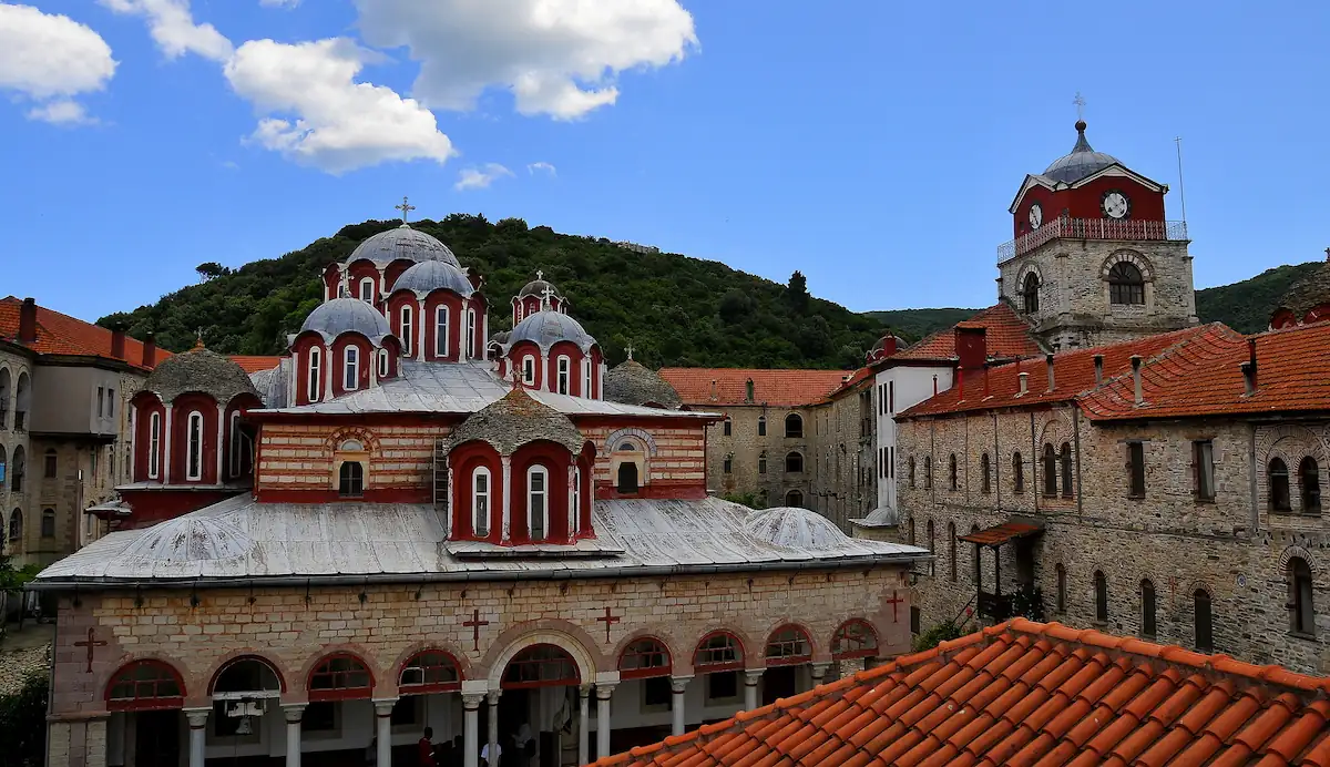 Esphigmenou Monastery Mount Athos Greece: Courtyard view of the Orthodox Esphigmenou Monastery church with traditional Byzantine architecture, domes, and stone walls under a blue sky.