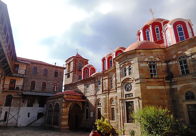 Wide-angle shot of the inner courtyard and the red-domed Catholicon church of the Konstamonitou Monastery in Mount Athos, Greece, under a cloudy sky.