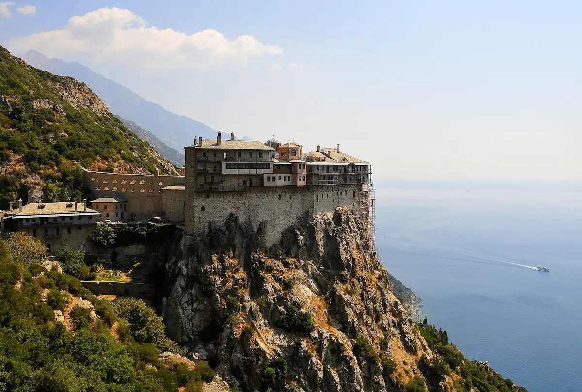 Panoramic view of Simonos Petra Monastery perched dramatically on a high rocky cliff overlooking the Aegean Sea under a clear sky in Mount Athos.