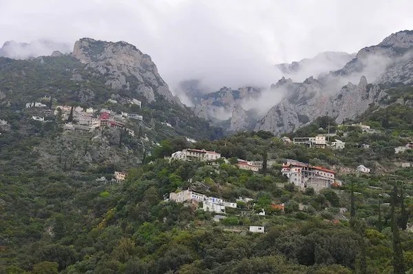 The traditional Eastern Orthodox Skete of Saint Anne nestled on the steep cliffs of Mount Athos under a cloudy sky.