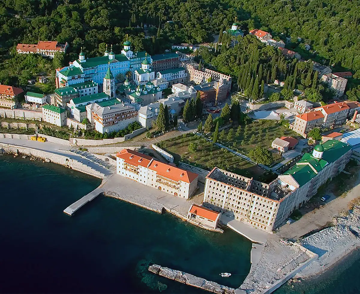 Aerial view of the St. Panteleimon Monastery with its distinctive green domes and large stone buildings on the coast of Mount Athos.